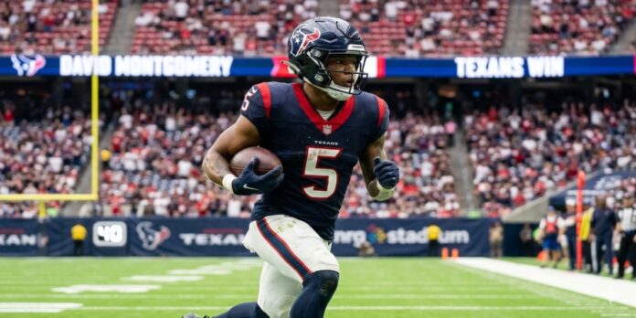 Running back David Montgomery running with a football while wearing a deep steel blue Houston Texans home jersey at NRG Stadium in 2026.
